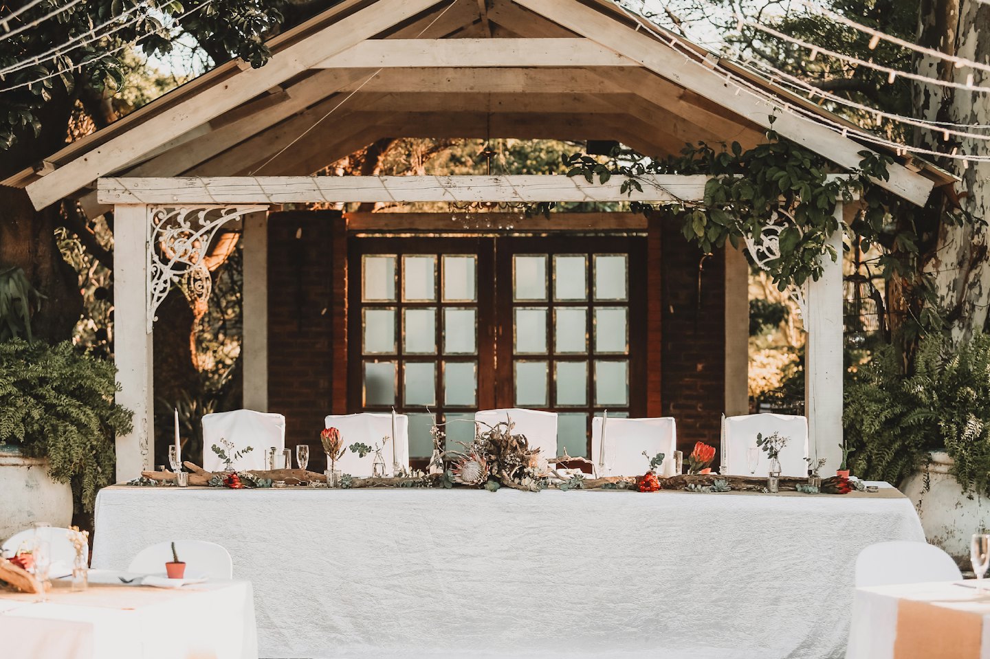 Wedding reception table set outdoors under a pergola with string lights.