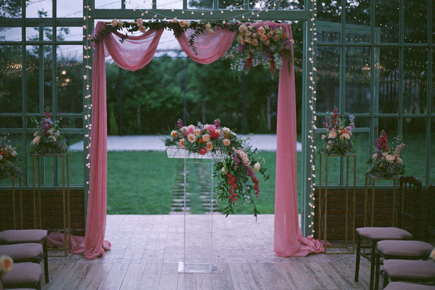 Wedding ceremony arch decorated with flowers in a glass greenhouse.