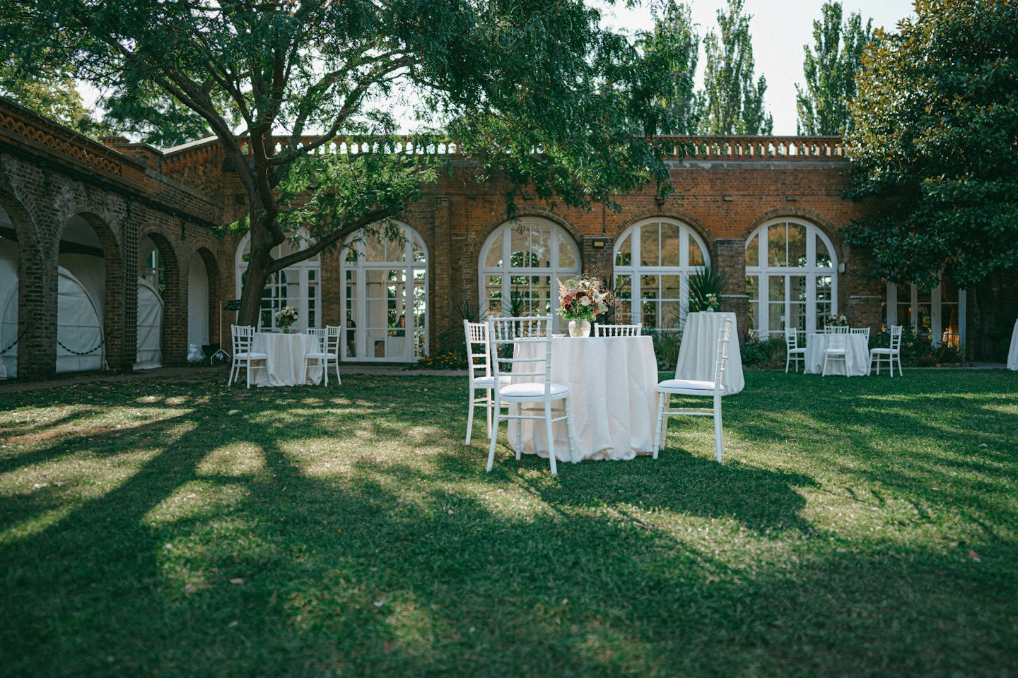 Round tables set for an event on a lawn by a historic building.