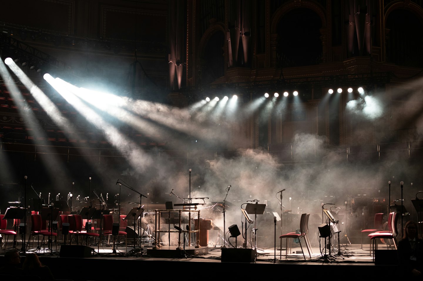 Empty orchestra stage with red chairs and music stands.